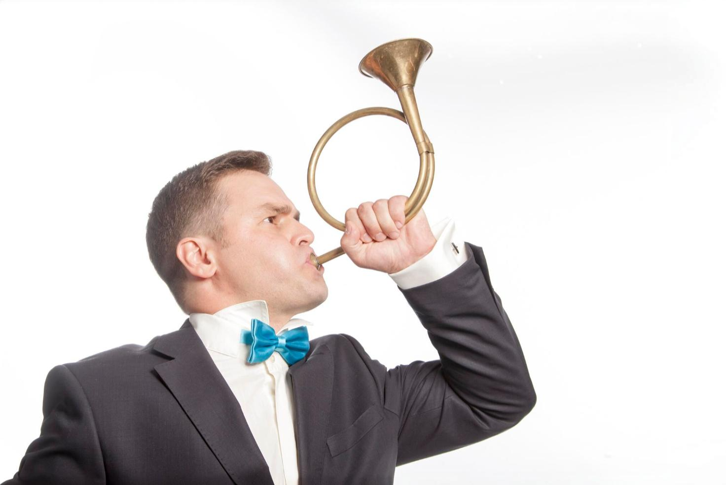 Man in a suit and bowtie blowing a french horn. Conveying business tooting their own horn. 