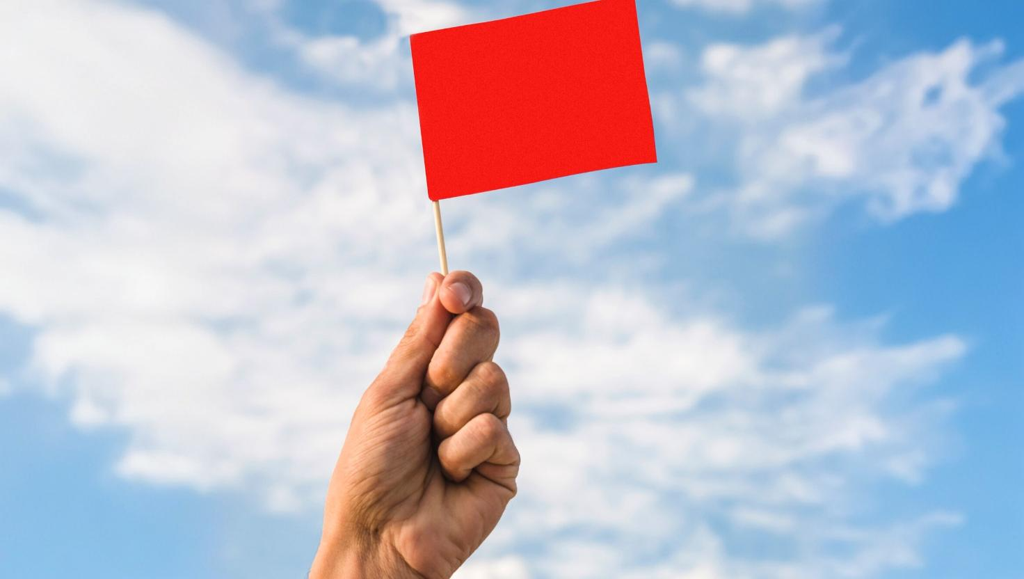 Hand holding a red flag, conveying warning signs hospitality business is using an outdated phone system.