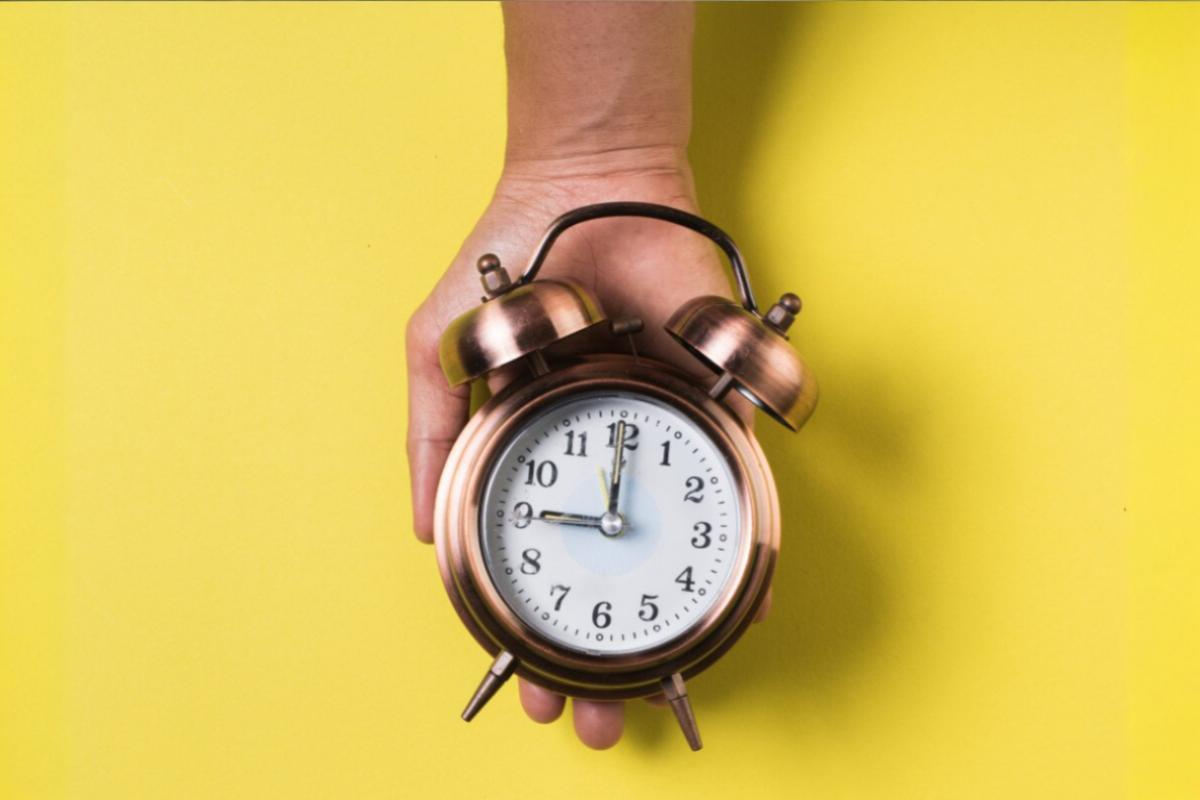 Hand holding clock against yellow background: example time of contact centers without omnichannel solutions.