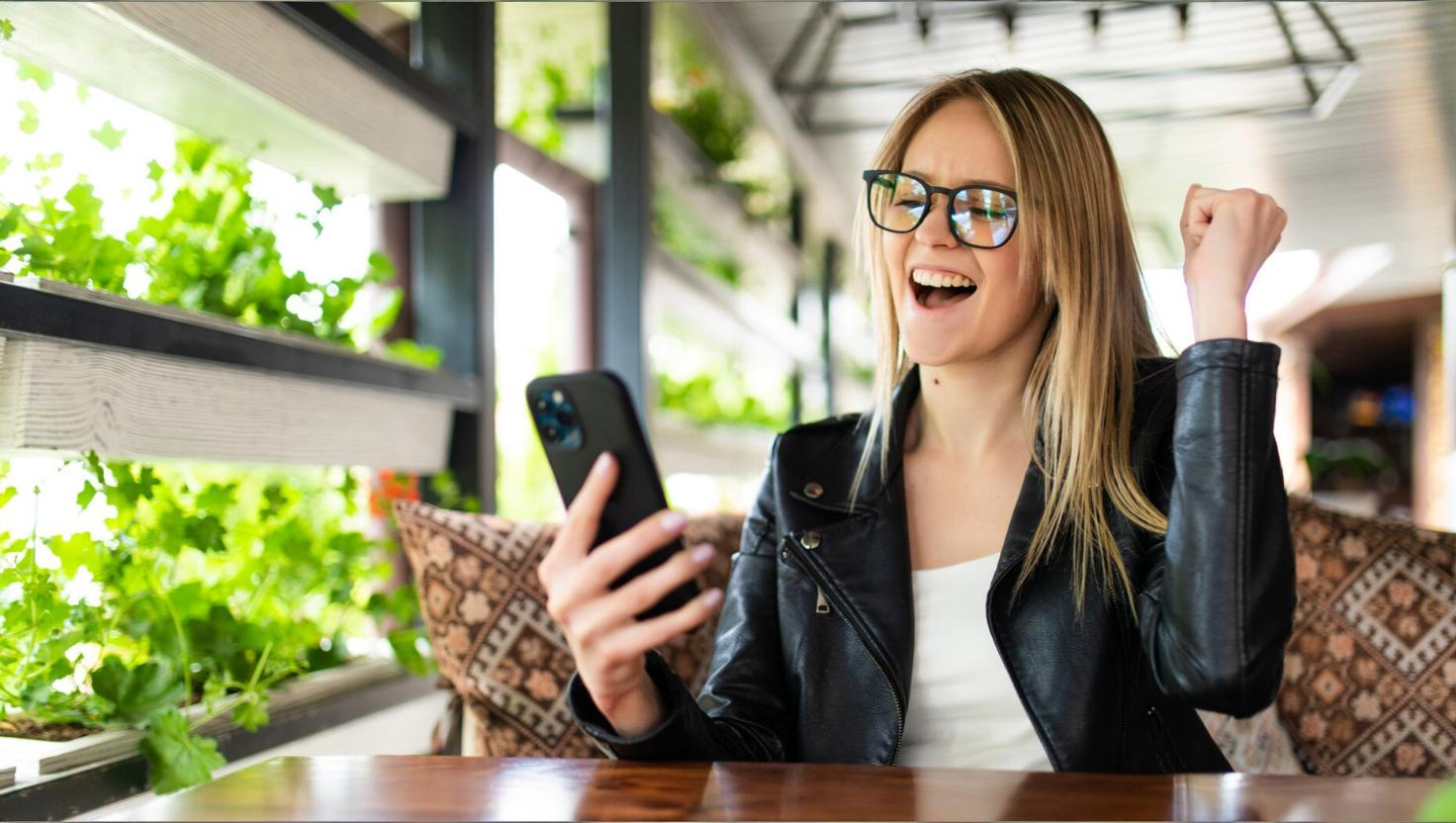Woman excitedly looking at phone sitting at table. Depicting omnichannel contact solution success..