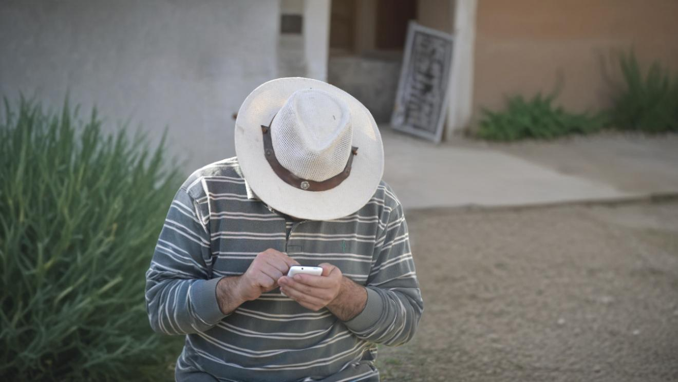 Man in a cowboy hat using a smartphone outdoors, representing improved contact center access and customer experience across all demographics.